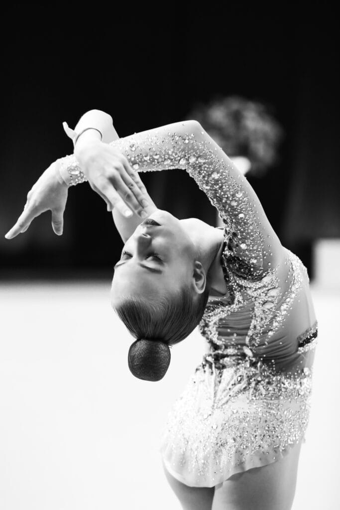 Iluvõimleja sooritamas kaunist painutust detailirohkes võistluskostüümis – elegants, painduvus ja kontroll esinemise hetkel.