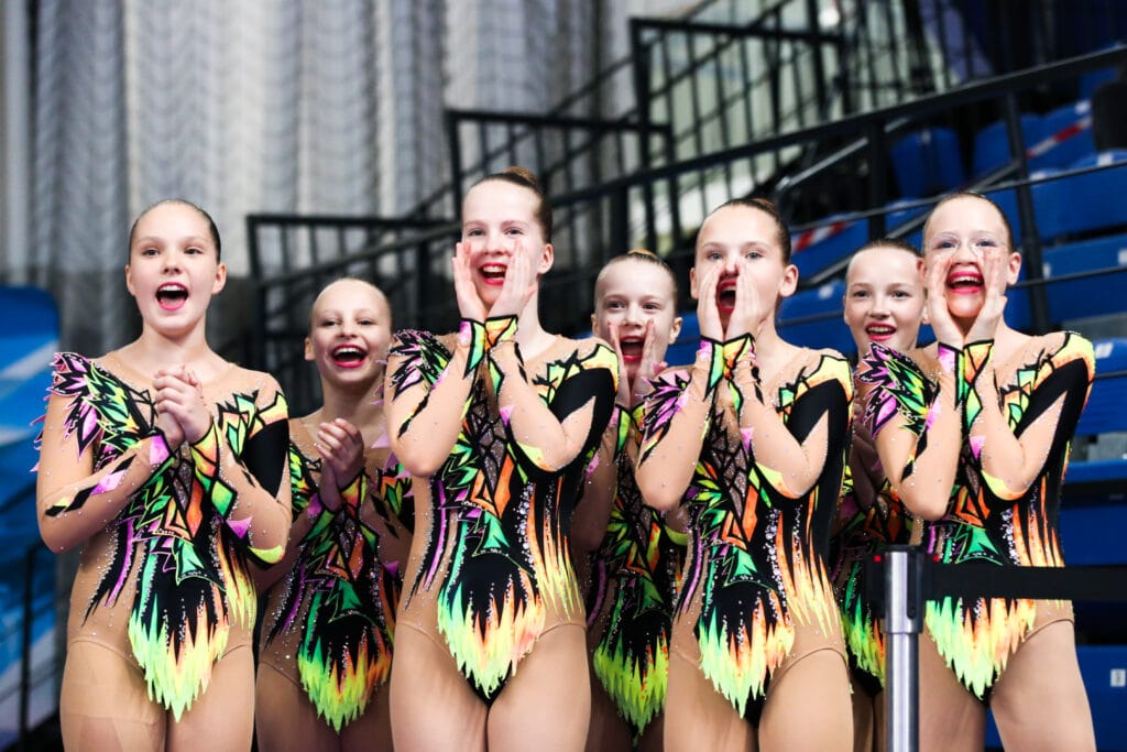 Noored iluvõimlejad tribüünil rõõmustamas ja kaasa elamas pärast võistlusesinemist – ühine emotsioon ja meeskonnavaim.