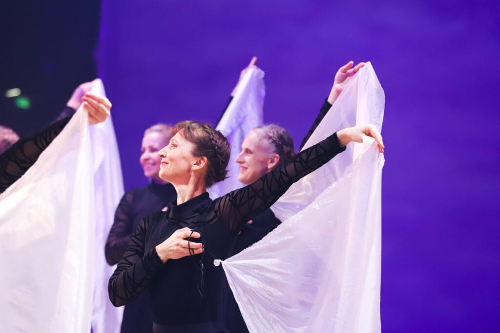 Võimlejad esitamas laval kangastega kava – rühmesinemine violetse valguse taustal